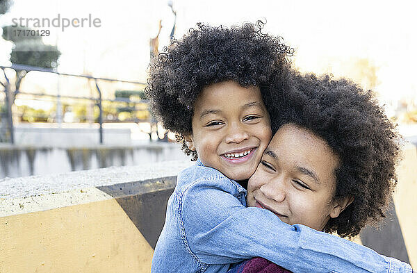 Lächelnde Geschwister  die sich gegenseitig umarmen  während sie im Park stehen