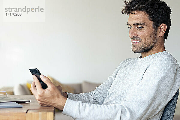 Mann benutzt Mobiltelefon  während er zu Hause sitzt