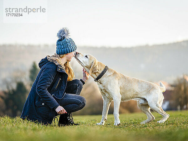 Young woman in knit hat playing with dog in field
