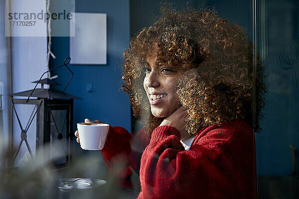 Thoughtful woman with coffee cup smiling while looking away sitting at cafe