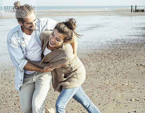 Fröhliches junges Paar  das am Wochenende am Strand spazieren geht und sich umarmt