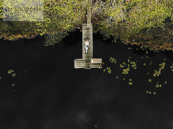 Luftaufnahme einer Frau  die auf einem Steg über einem See im Wald liegt