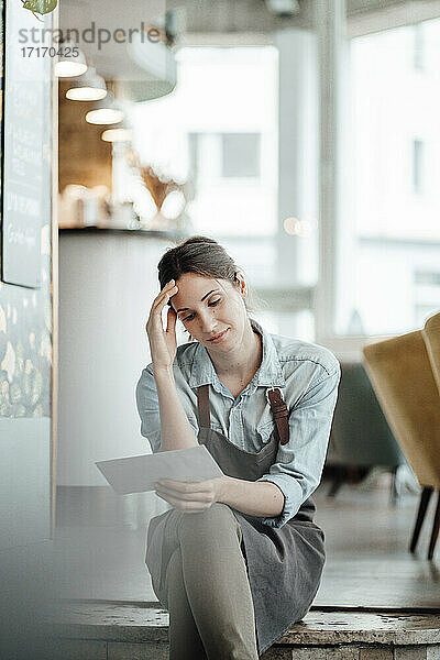 Weibliche Unternehmerin betrachtet Papier  während sie in einem Kaffee sitzt