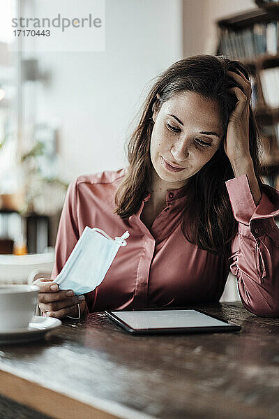 Weibliche Fachkraft mit Hand im Haar bei der Nutzung eines digitalen Tablets in einem Café