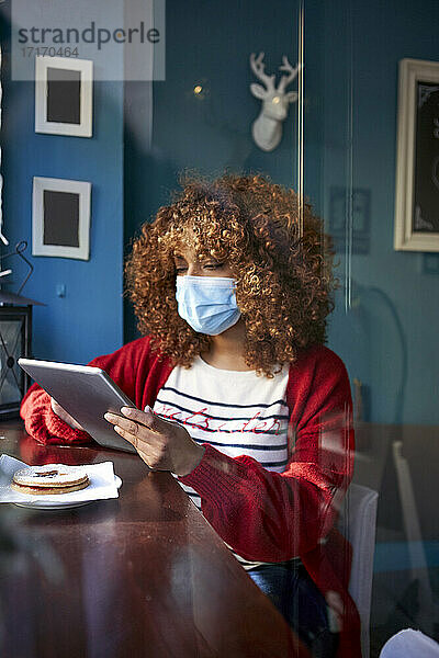 Woman wearing sanitary mask using digital tablet while sitting at home