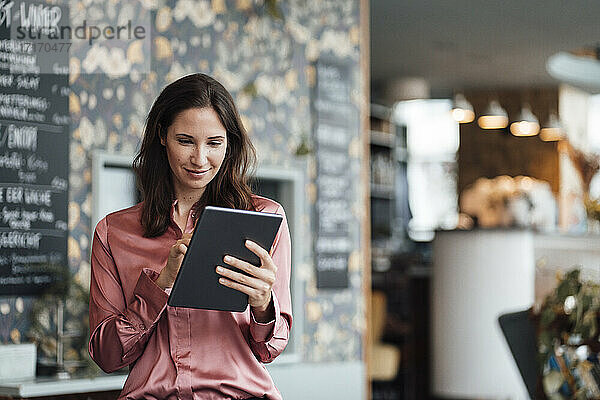 Lächelnde Freiberuflerin bei der Arbeit am digitalen Tablet im Café