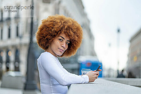 Curly hair woman using mobile phone while standing outdoors