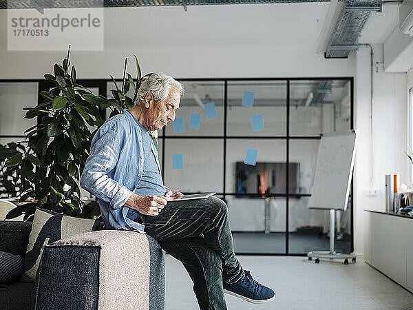 Geschäftsmann  der ein digitales Tablet benutzt  während er auf dem Sofa im Büro sitzt