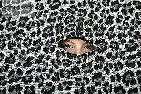 Eyes of teenage girl peeking through hole in leopard print pattern