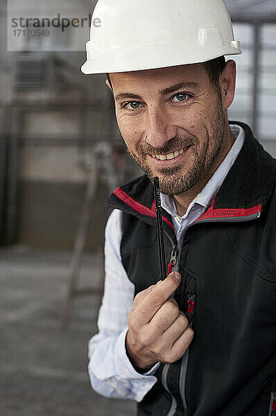 Nahaufnahme eines lächelnden männlichen Architekten mit Helm auf einer Baustelle