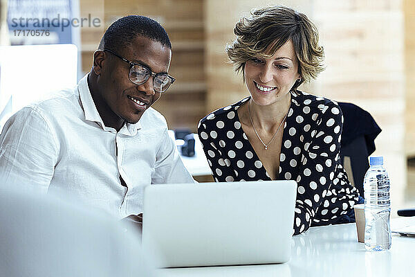 Männliche und weibliche Kollegen benutzen einen Laptop  während sie am Schreibtisch im Büro sitzen