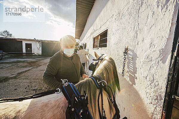 Expertise wearing face mask standing by horse at stable