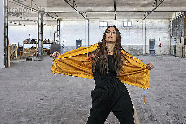 Confident female modern dancer in yellow jacket at abandoned factory
