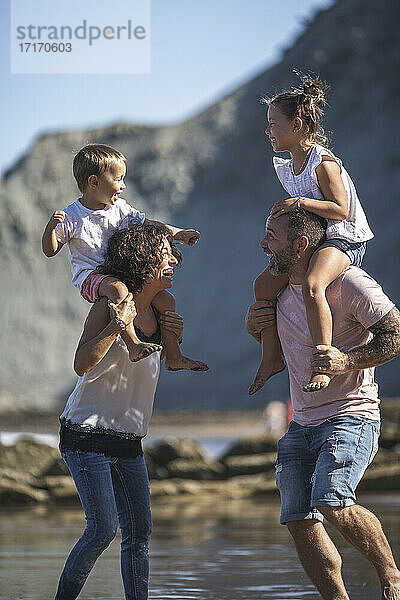 Cheerful parents with kids on shoulder enjoying at beach