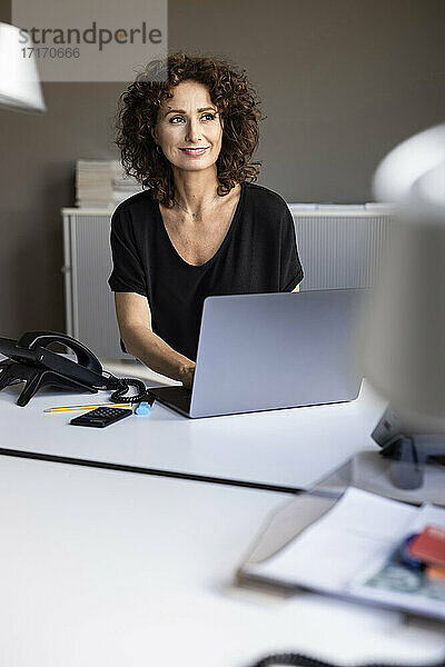 Nachdenkliche Geschäftsfrau lächelt  während sie im Büro sitzt