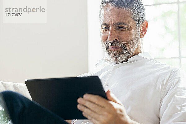 Lächelnder Geschäftsmann  der zu Hause sitzend an einem digitalen Tablet arbeitet