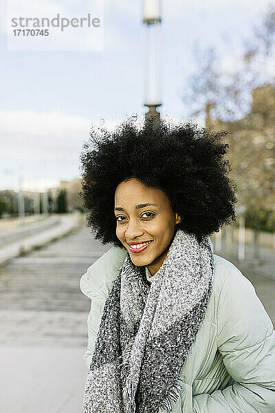 Lächelnde Afro-Frau mit Händen in den Taschen  die im Winter im Freien steht