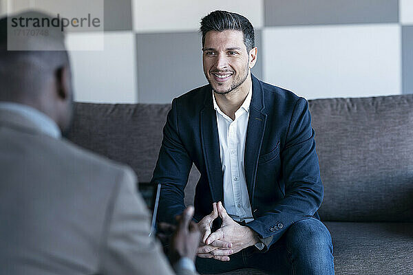 Smiling businessman looking at colleague while sitting at office