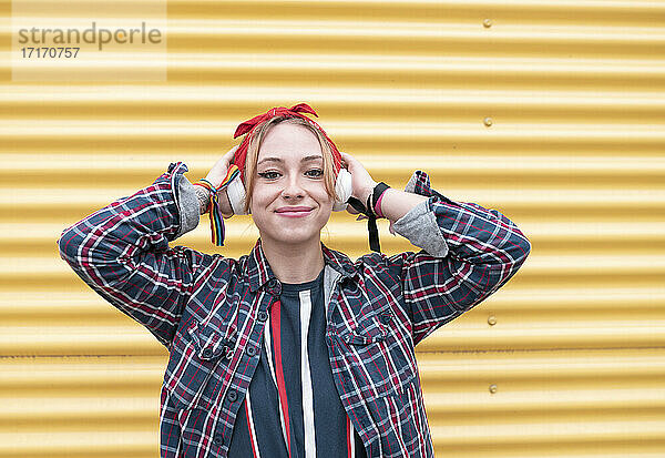 Frau mit Kopfhörern  die lächelnd an einer gelben Wand steht