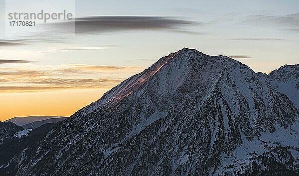 Rocky mountain covered in snow against cloudy sky during sunset