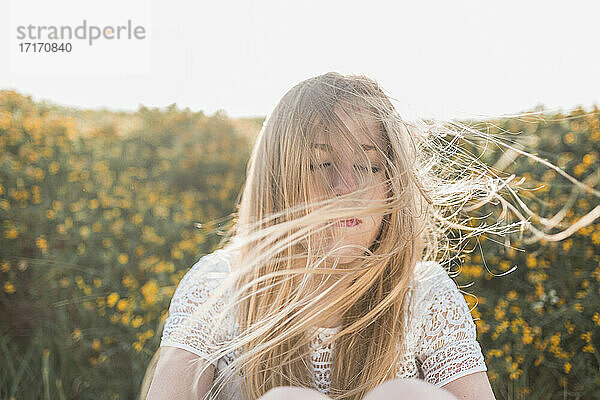 Der Wind bläst das Haar einer jungen Frau  die auf einem landwirtschaftlichen Feld sitzt