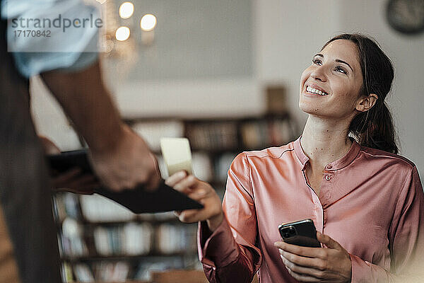 Lächelnder weiblicher Kunde  der mit Kreditkarte an einen männlichen Kellner in einem Café zahlt