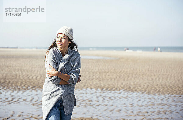 Junge Frau in Strickjacke beim Strandspaziergang nachdenklich