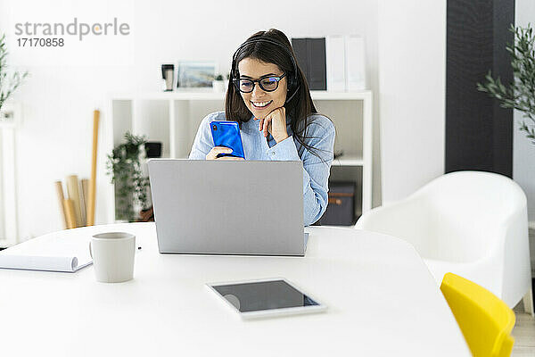Lächelnde Geschäftsfrau  die ein Mobiltelefon benutzt  während sie im Büro sitzt