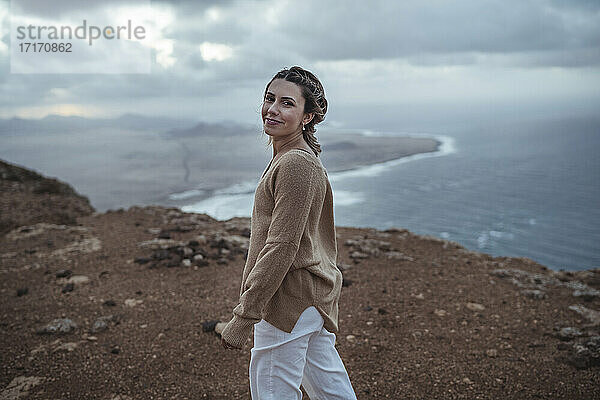 Junge Frau lächelt beim Spaziergang auf dem Berg vor dem Strand von Famara  Lanzarote  Spanien