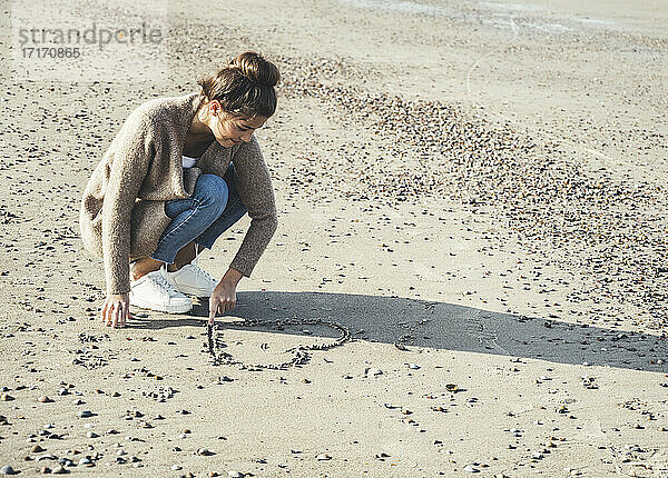 Junge Frau zeichnet Herz auf Sand am Strand