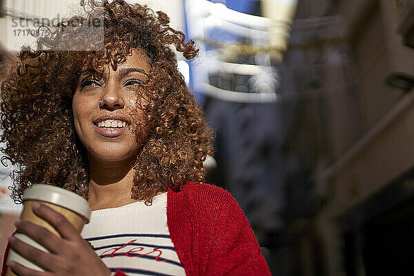Afro woman with disposable coffee cup looking away while standing outdoors