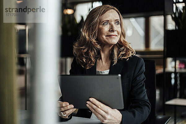 Nachdenkliche Geschäftsfrau mit digitalem Tablet  die im Büro wegschaut