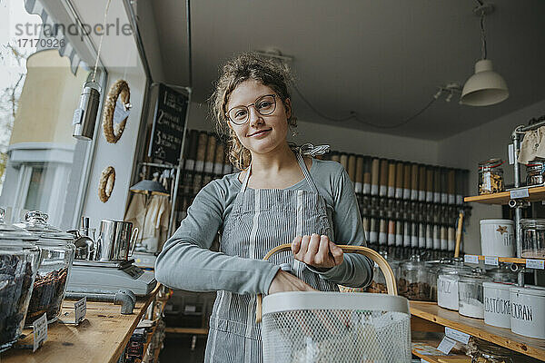 Lächelnde Verkäuferin  die einen Korb hält  während sie in einem Zero-Waste-Shop arbeitet