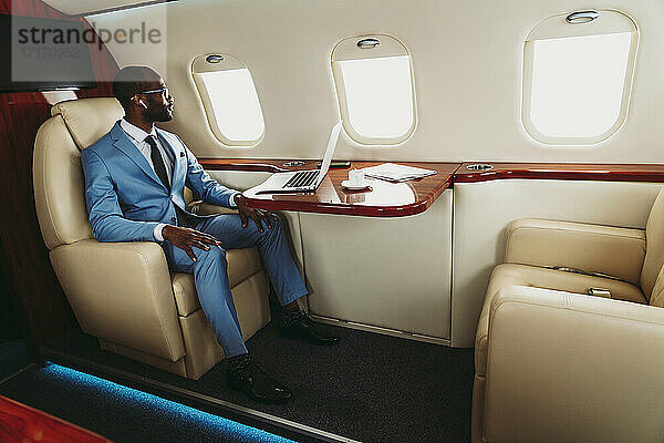 Geschäftsmann schaut durch das Fenster mit Laptop auf dem Tisch im Flugzeug