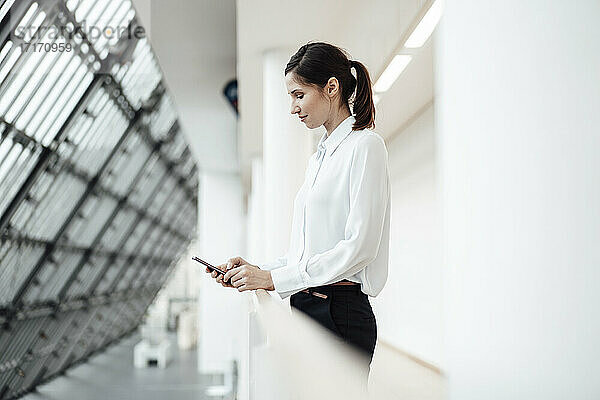 Unternehmerin  die im Bürokorridor eine SMS auf ihrem Smartphone schreibt