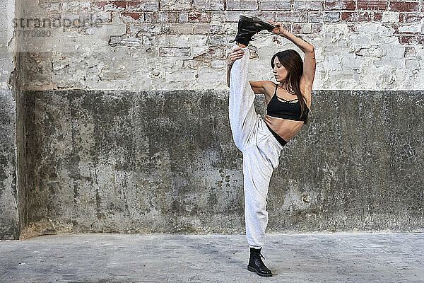 Female dancer standing on one leg against weathered wall in factory