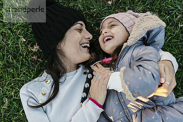 Lächelnde Mutter mit Strickmütze  die mit ihrer Tochter spielt  während sie im Gras liegt
