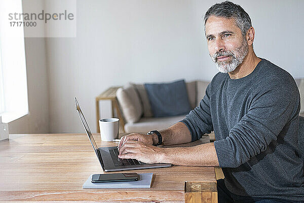 Geschäftsmann mit Laptop  der wegschaut  während er zu Hause im Büro sitzt