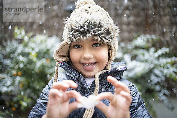 Cute smiling girl holding flower during snowfall