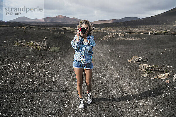 Junger Tourist steht mit Kamera auf dem Fußweg am Vulkan El Cuervo  Lanzarote  Spanien