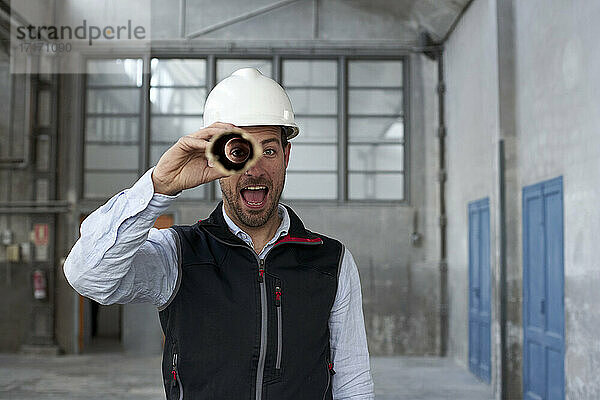 Männlicher Architekt mit offenem Mund  der durch einen Karton schaut  während er in einem Gebäude steht