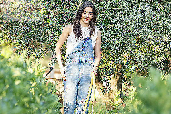 Smiling female with hand in pocket watering plants in backyard