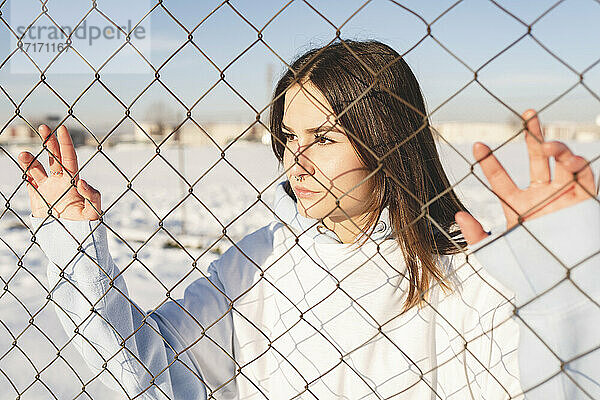 Young woman looking away while standing behind fence