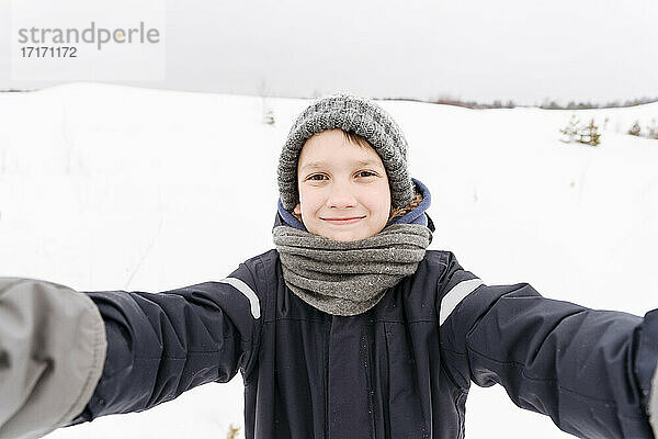 Lächelnder Junge auf schneebedeckter Landschaft gegen den Himmel stehend