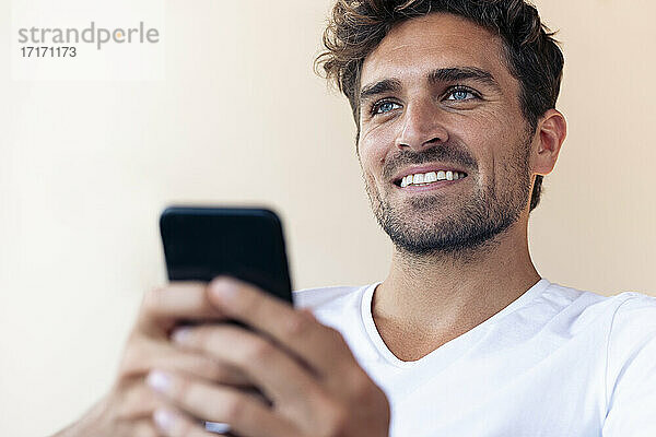 Gut aussehender Mann  der lächelt  während er sein Smartphone zu Hause benutzt