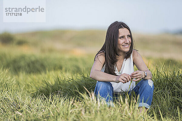 Schöne junge Frau schaut weg  während sie im Gras sitzt