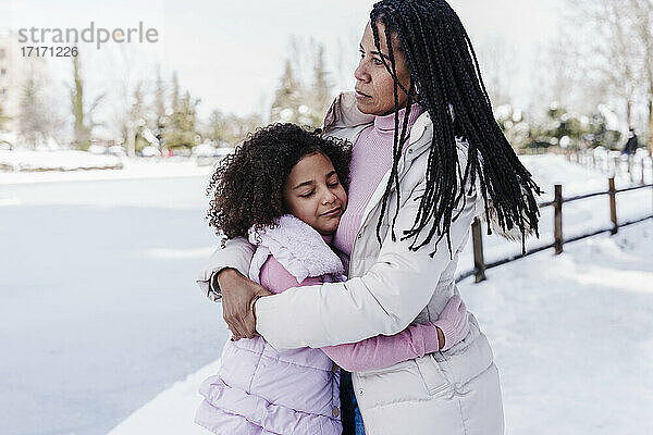 Tochter  die ihre Mutter umarmt  während sie im Schnee im Park steht