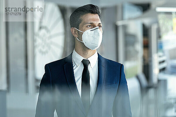 Geschäftsmann mit Gesichtsschutzmaske  der wegschaut  während er im Büro steht