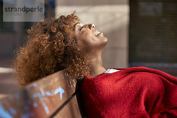 Smiling woman with eyes closed resting while leaning on bench