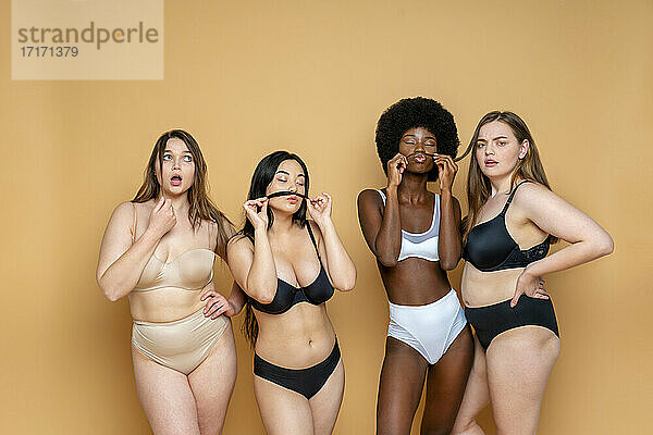 Multi-ethnische Gruppe von weiblichen Modellen in Dessous stehen vor gelbem Hintergrund